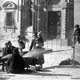 Caldarrostaia in Piazza Grande attorniata da donne e bambini. Dietro, la parte inferiore della facciata del Palazzetto della Fraternita.