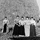 Gruppo di donne e bambine davanti ai pagliai. A sinistra, una contadina con due mezzine di rame.